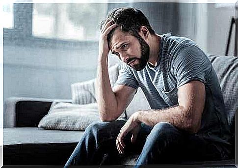 A man is sitting on the couch with his hand in his hair