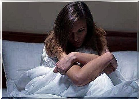 A woman sits up in bed with her arms over her knees